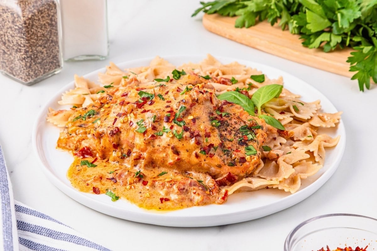 Chicken in creamy sauce with herbs, served over bow tie pasta on a white plate.
