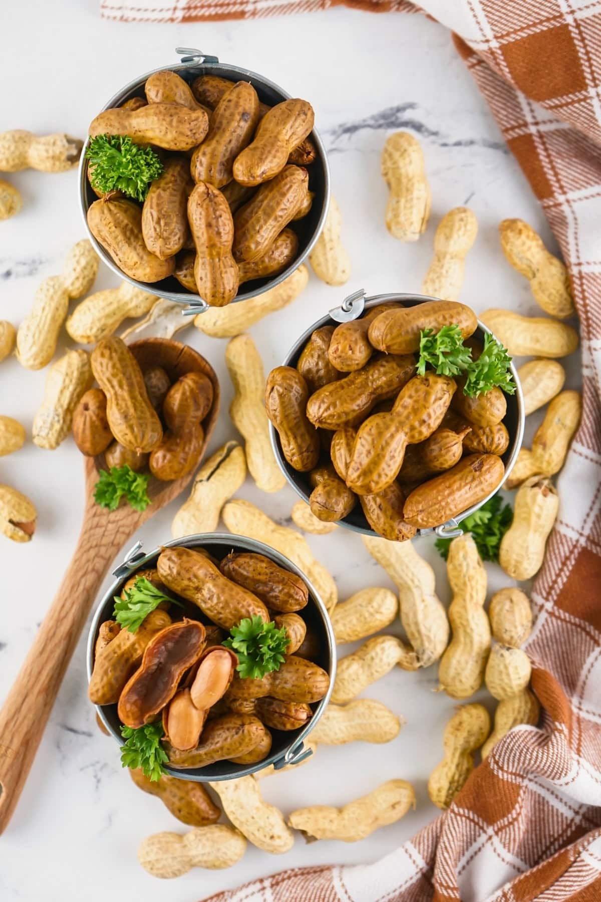 Three small buckets of boiled peanuts with parsley, surrounded by peanut shells.