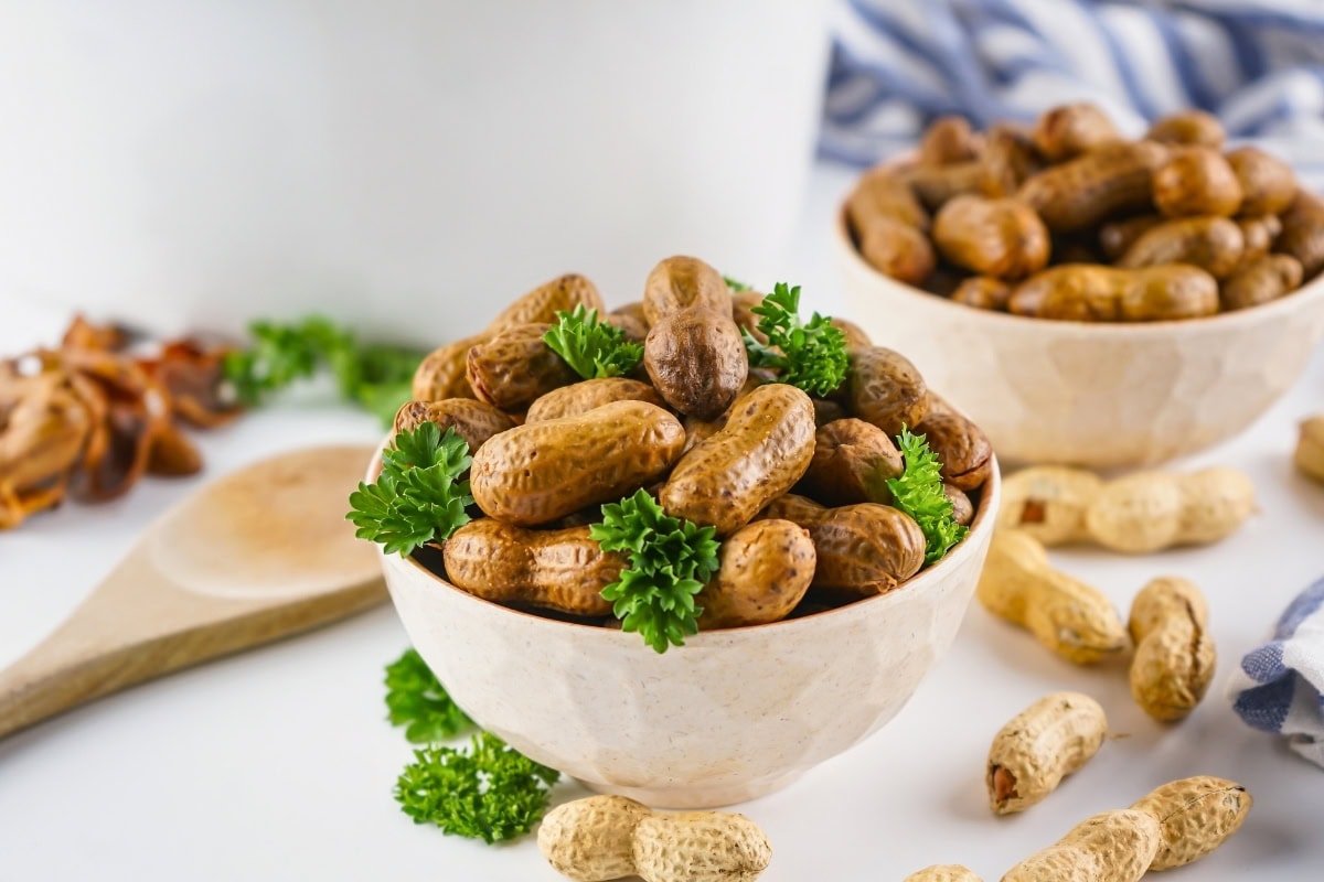 Boiled peanuts in a bowl, garnished with parsley, with more peanuts nearby.