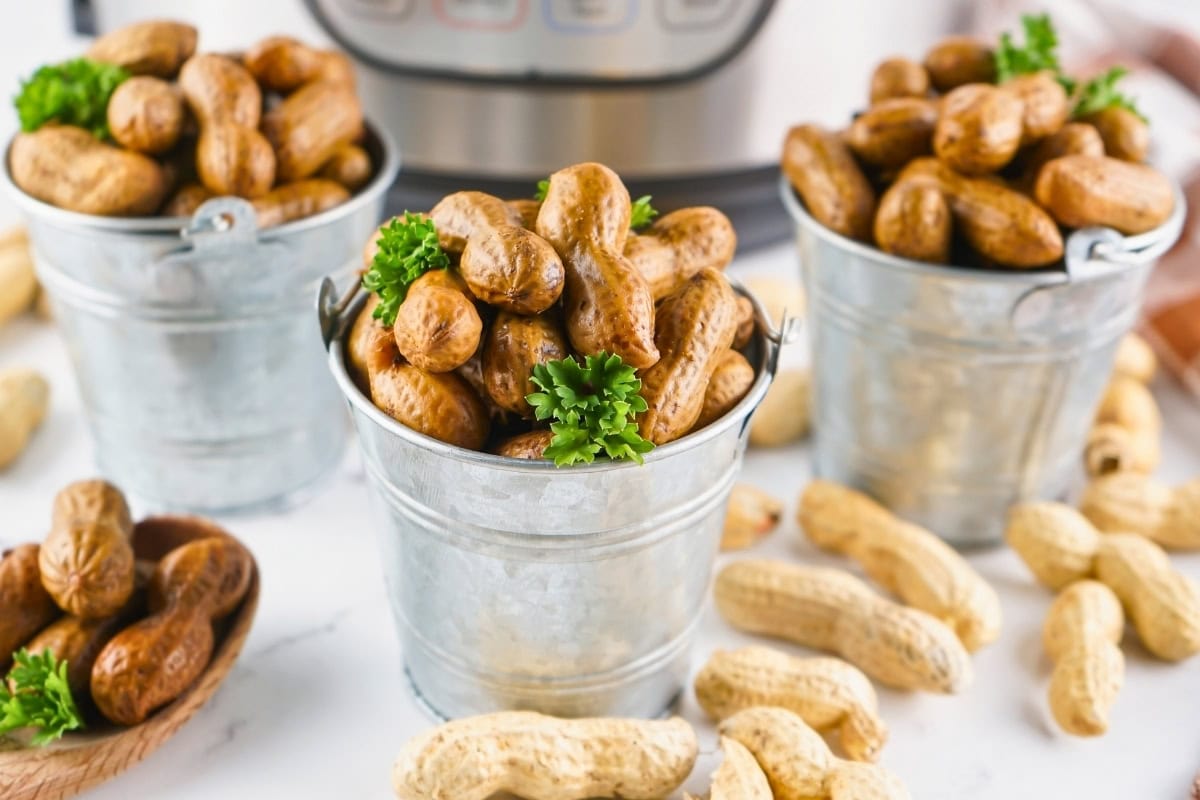 Three metal buckets filled with boiled peanuts, garnished with parsley.