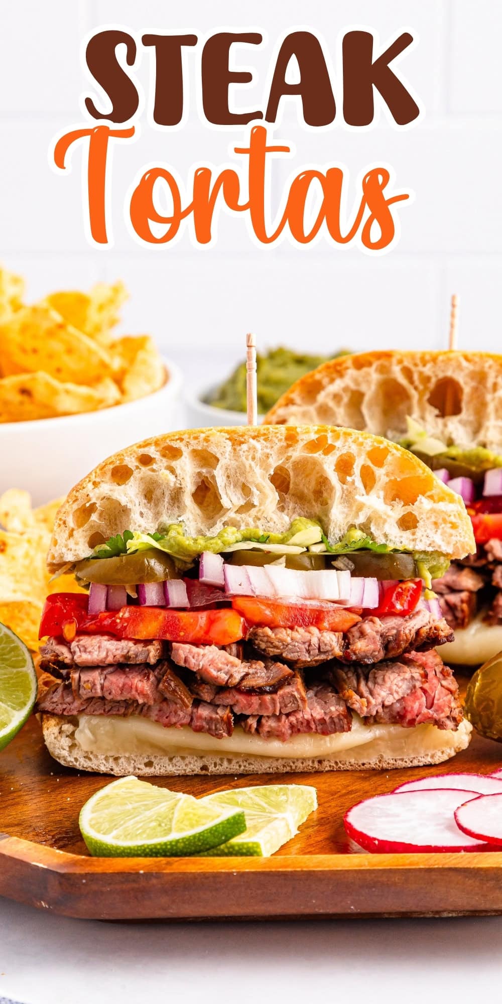 Steak torta sandwiches with veggies on a wooden board, lime slices, and chips.
