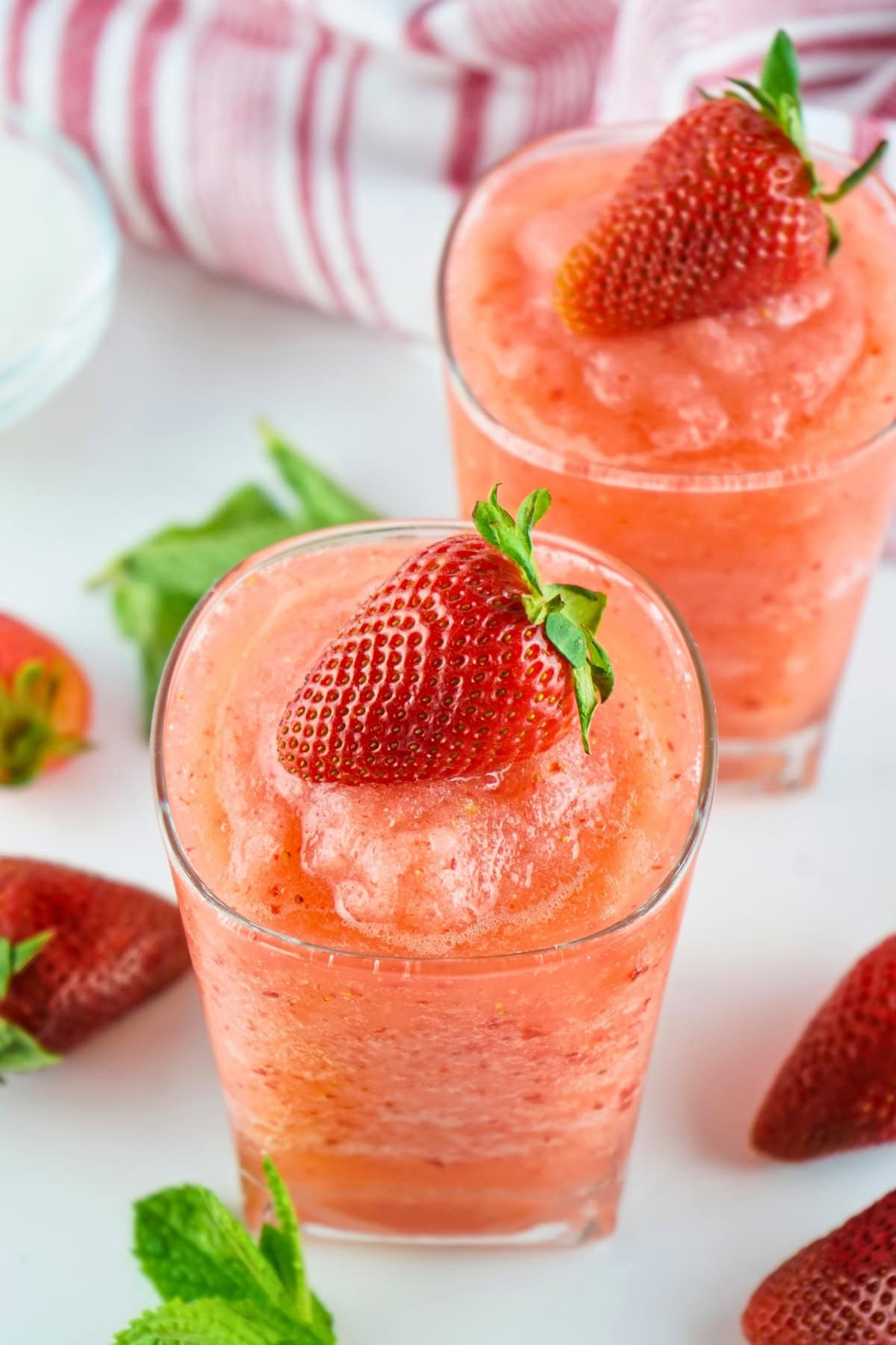 Two glasses of strawberry slush topped with fresh strawberries and mint leaves.