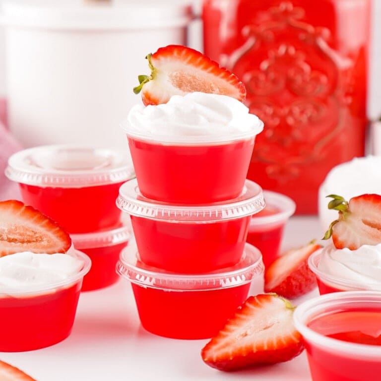Red gelatin cups topped with whipped cream and strawberry slices, stacked neatly.
