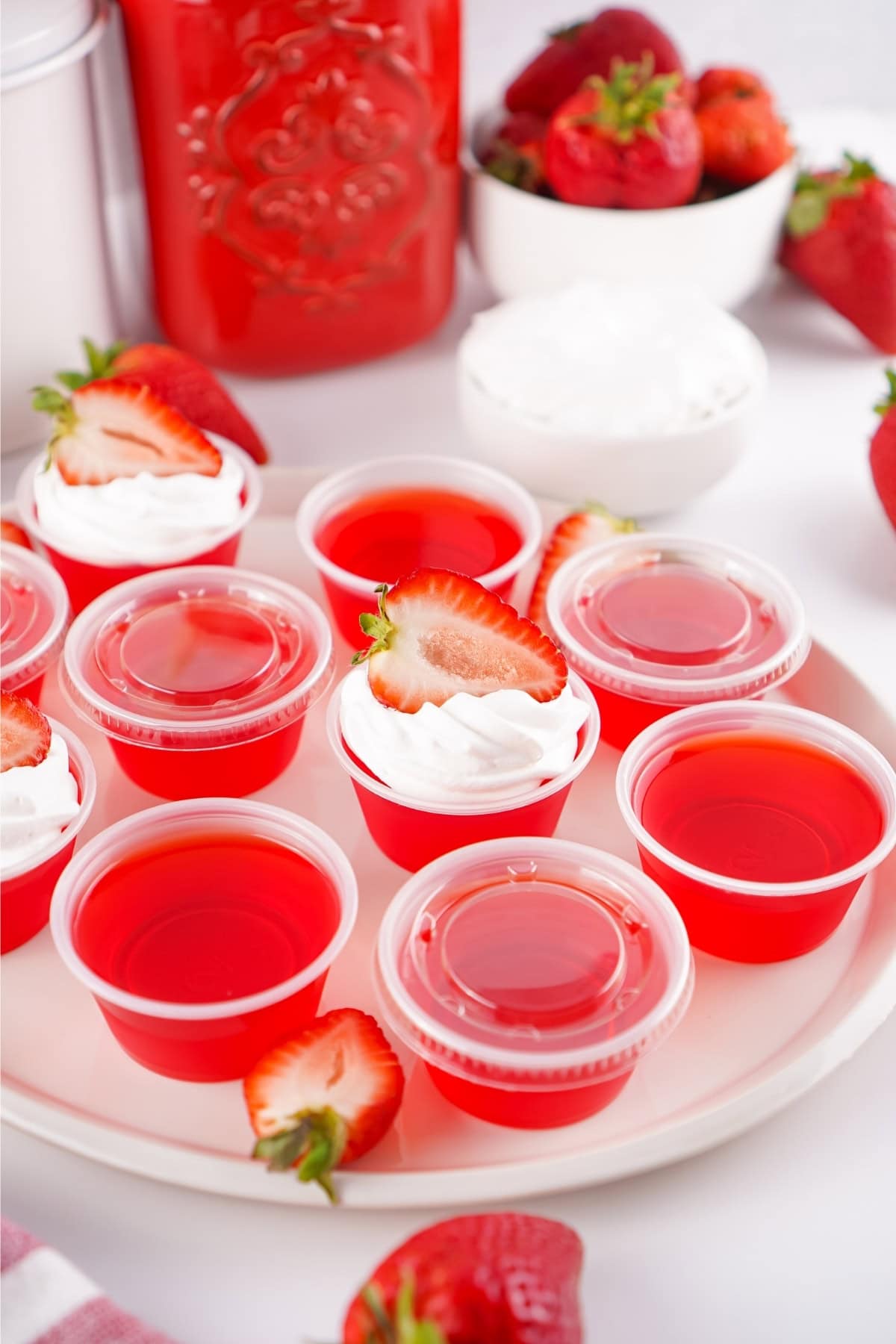 Red gelatin cups topped with whipped cream and strawberry slices on a white plate.