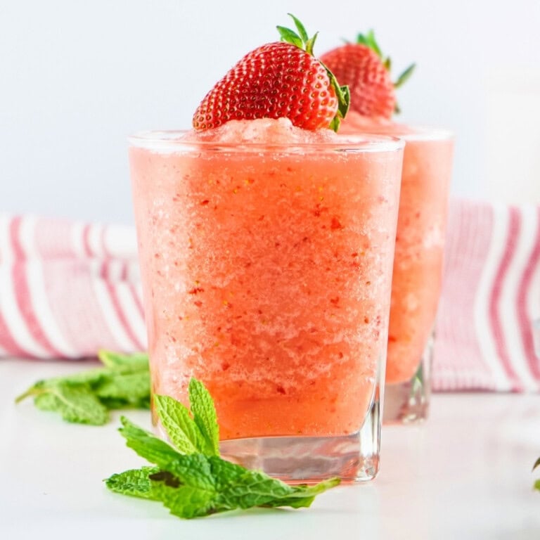 Two strawberry slushies topped with fresh strawberries and mint leaves.
