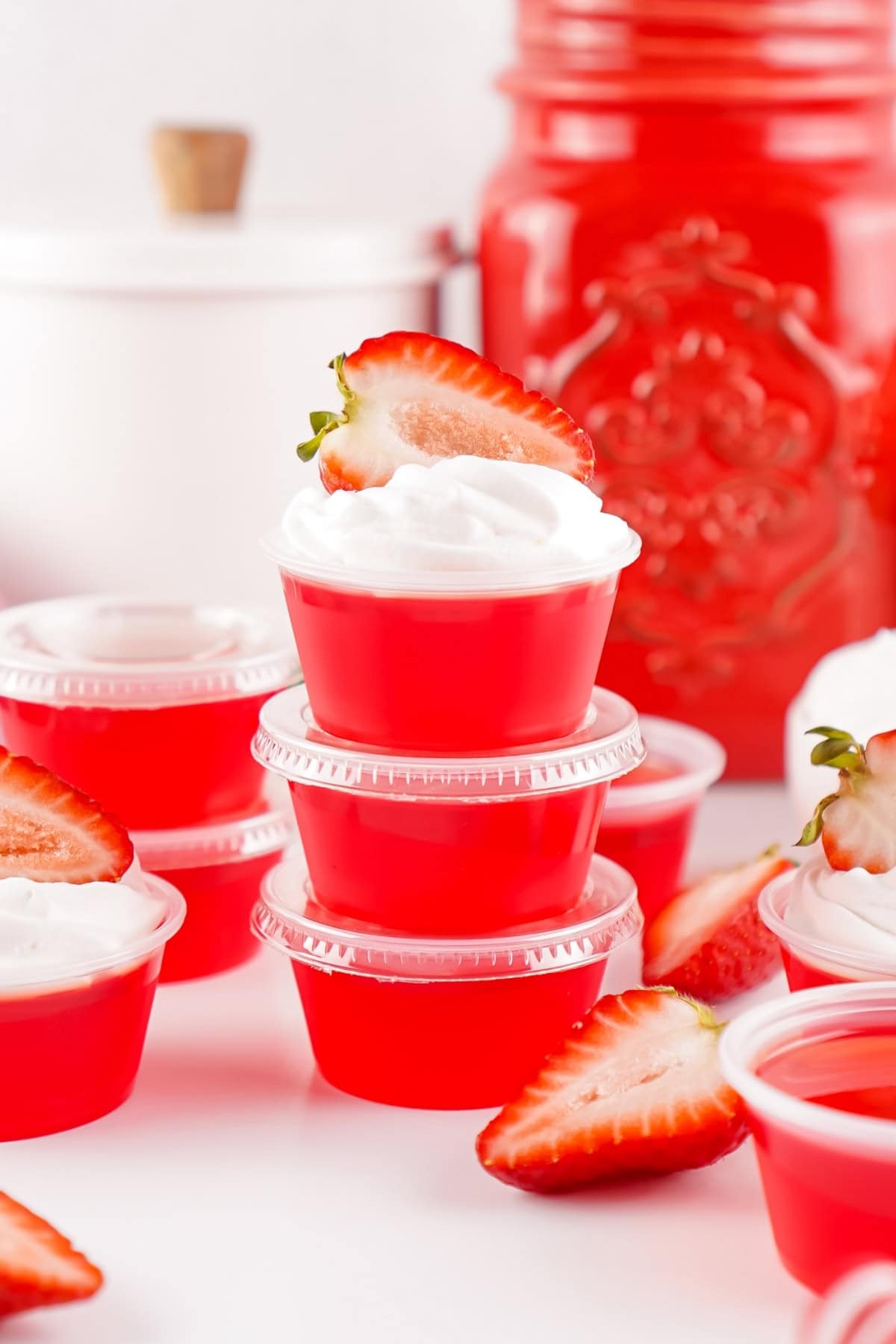 Red gelatin cups topped with whipped cream and strawberries, stacked on a table.