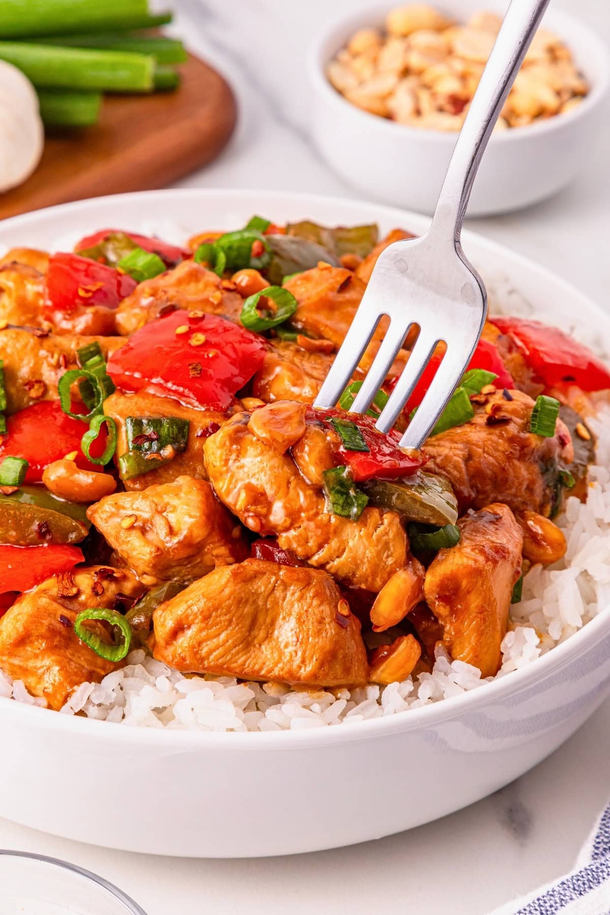 A fork lifts kung pao chicken with vegetables over white rice in a bowl.