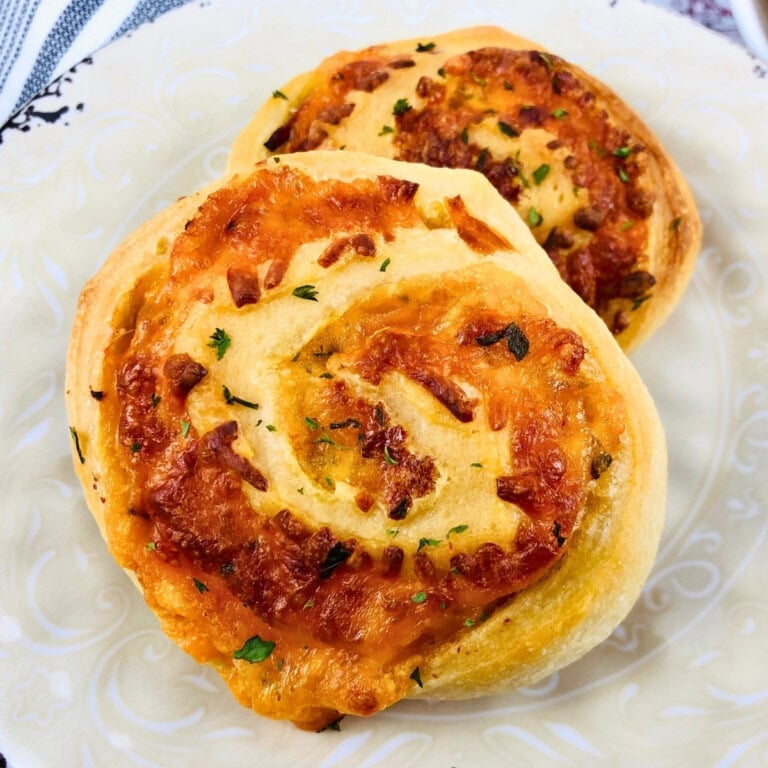 Two cheesy, golden-brown pinwheel pastries on a white decorative plate.