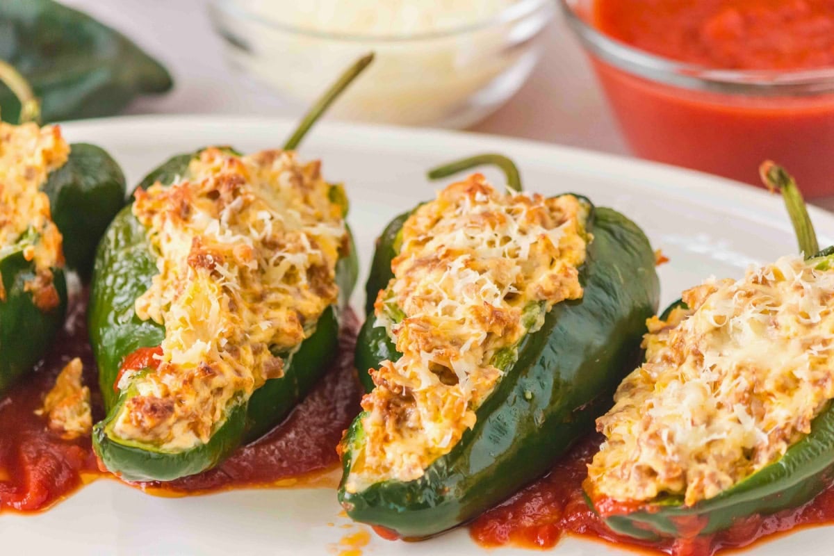 Four stuffed poblano peppers topped with cheese on a plate with tomato sauce.