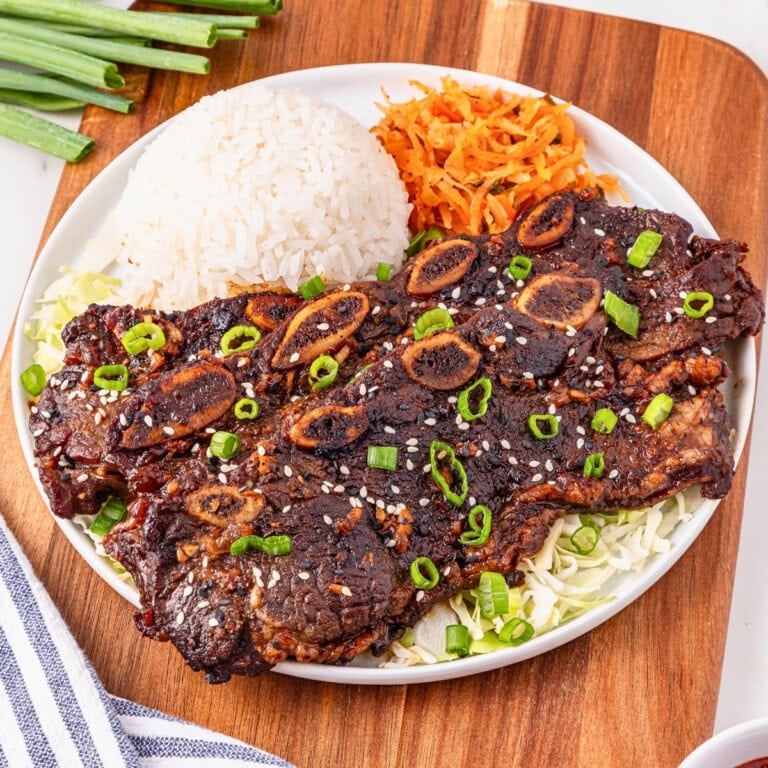 Plate of grilled Korean short ribs with rice, shredded carrots, and green onions.
