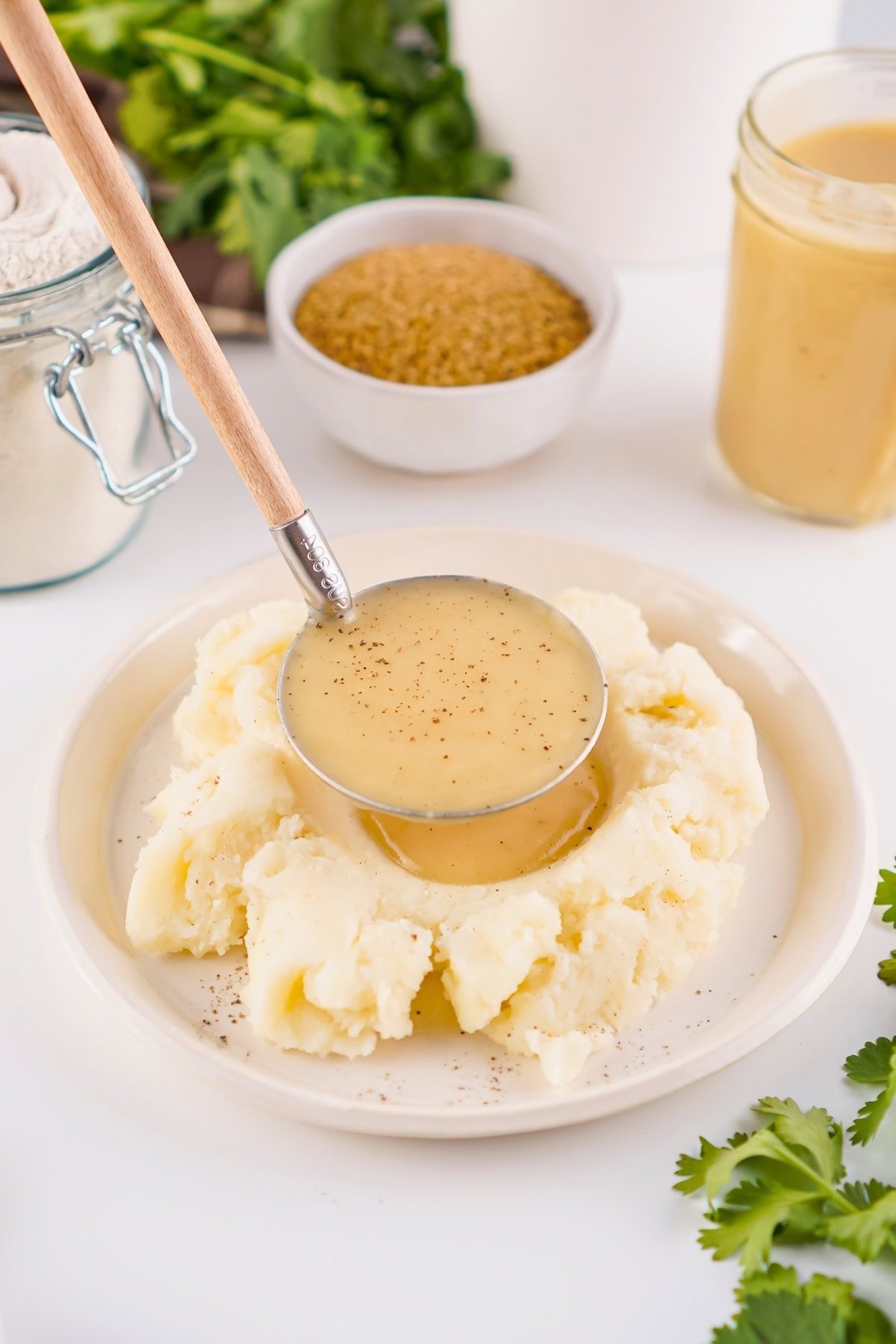 A ladle pours gravy onto mashed potatoes on a white plate.