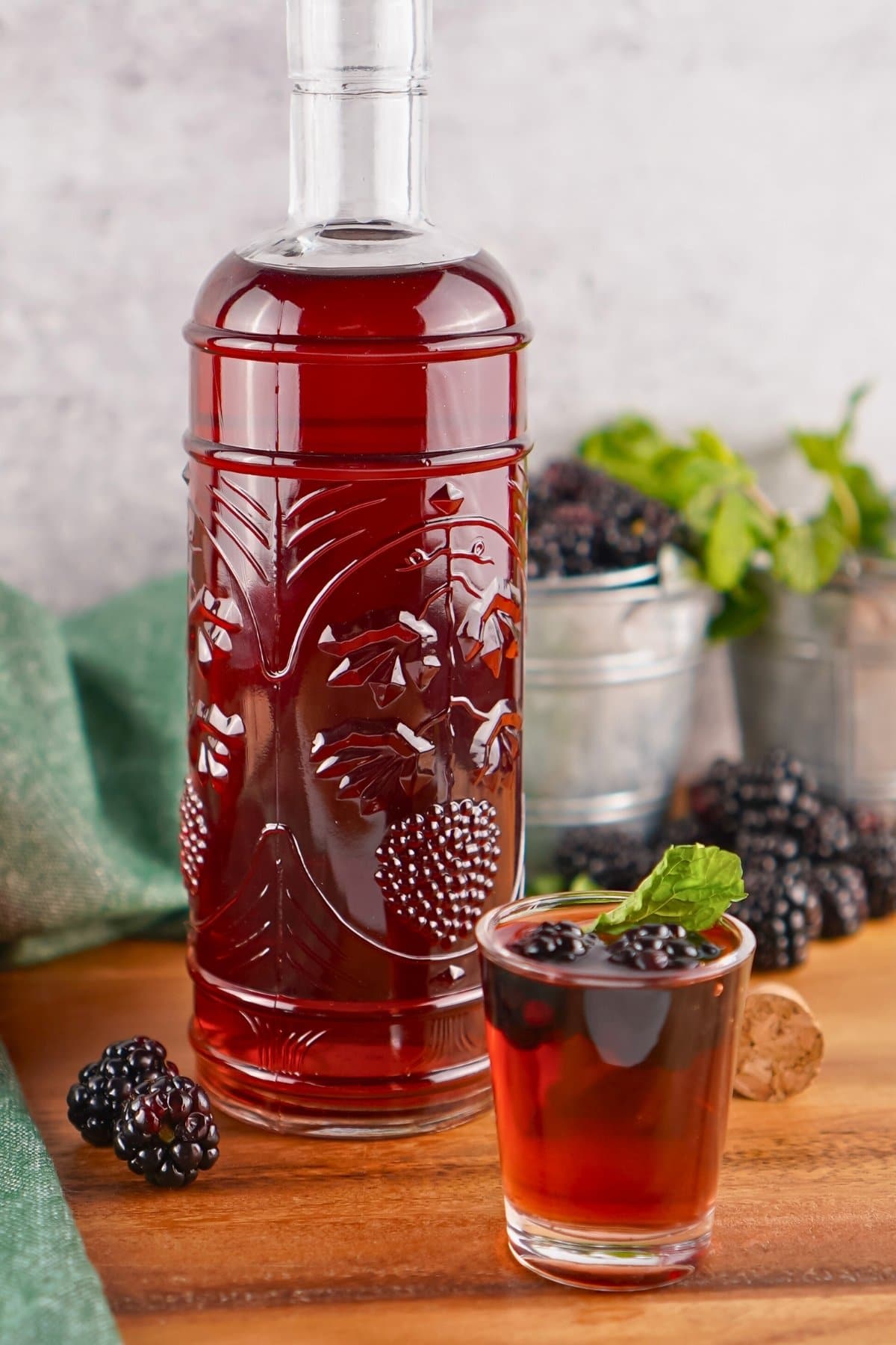 A bottle and shot glass of blackberry liqueur with fresh blackberries and mint.