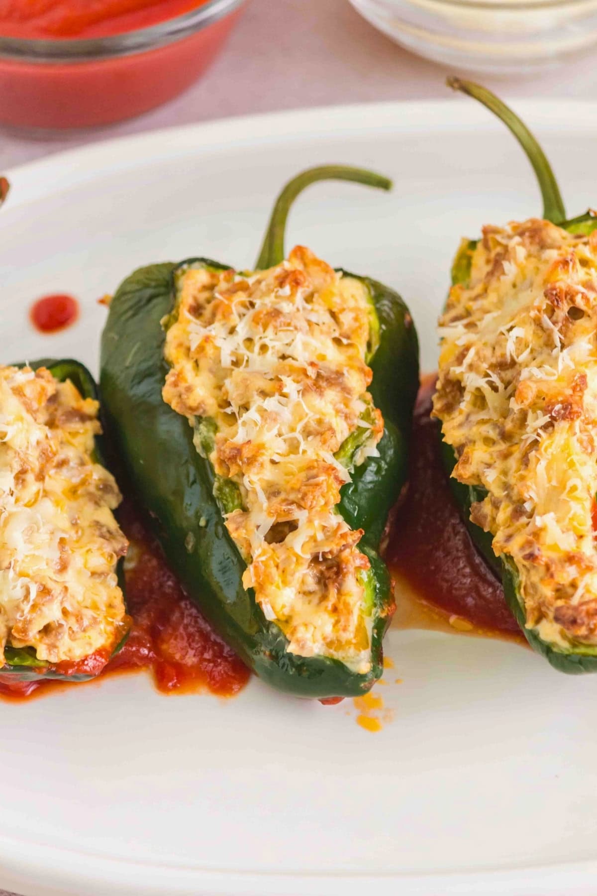 Three stuffed poblano peppers topped with melted cheese on a white plate with sauce.