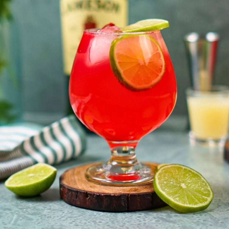 An Irish Redhead cocktail with lime slices in a glass on a wooden coaster.