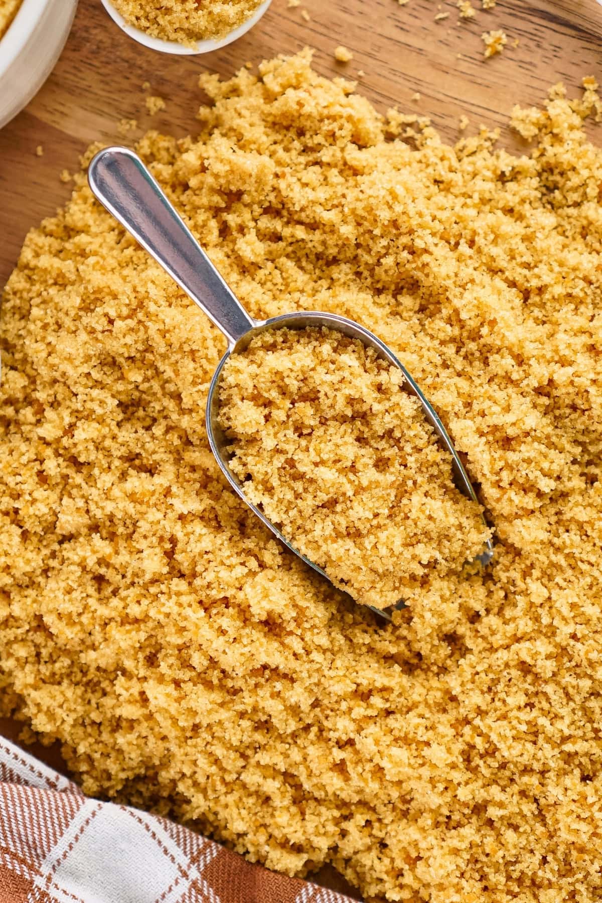 A metal scoop in a pile of brown sugar on a wooden surface.