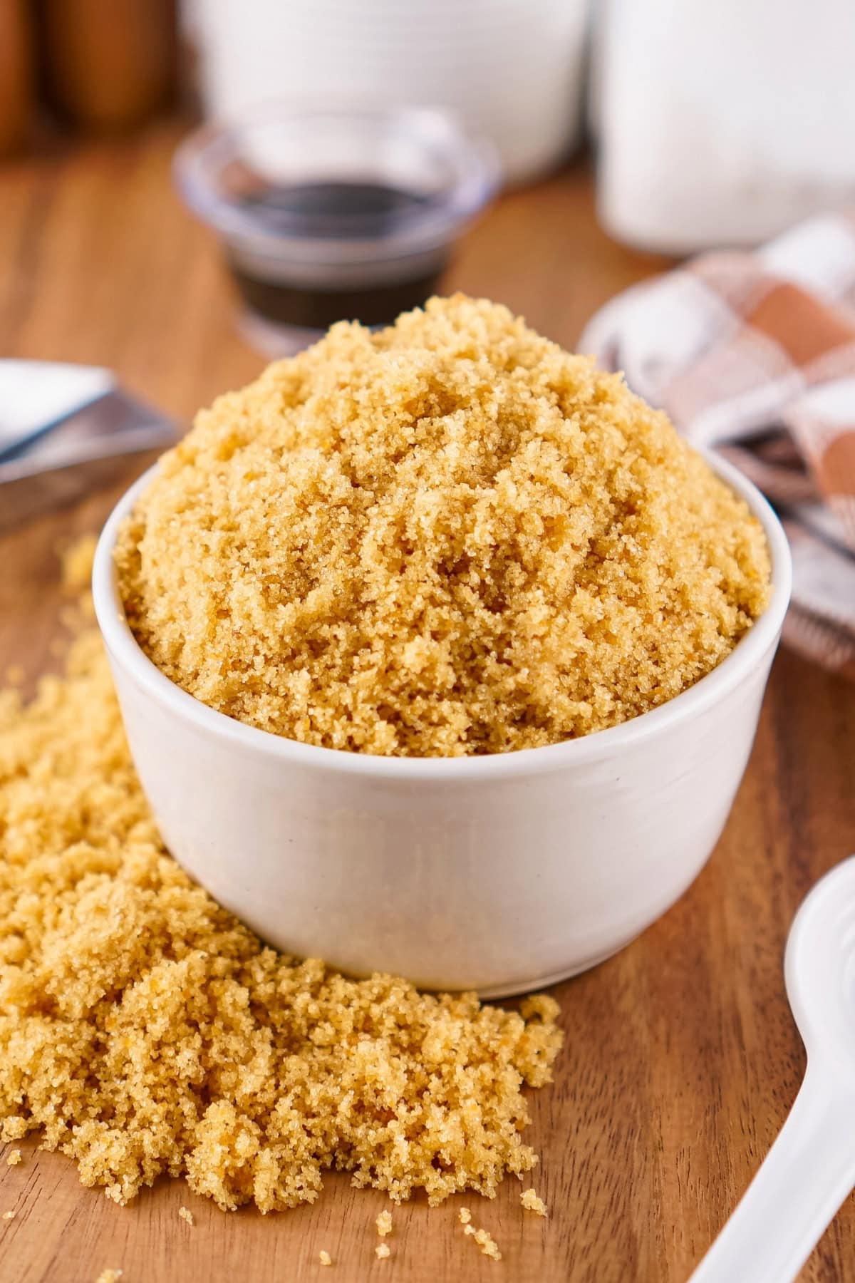 A white bowl filled with brown sugar, with some spilled on a wooden surface.