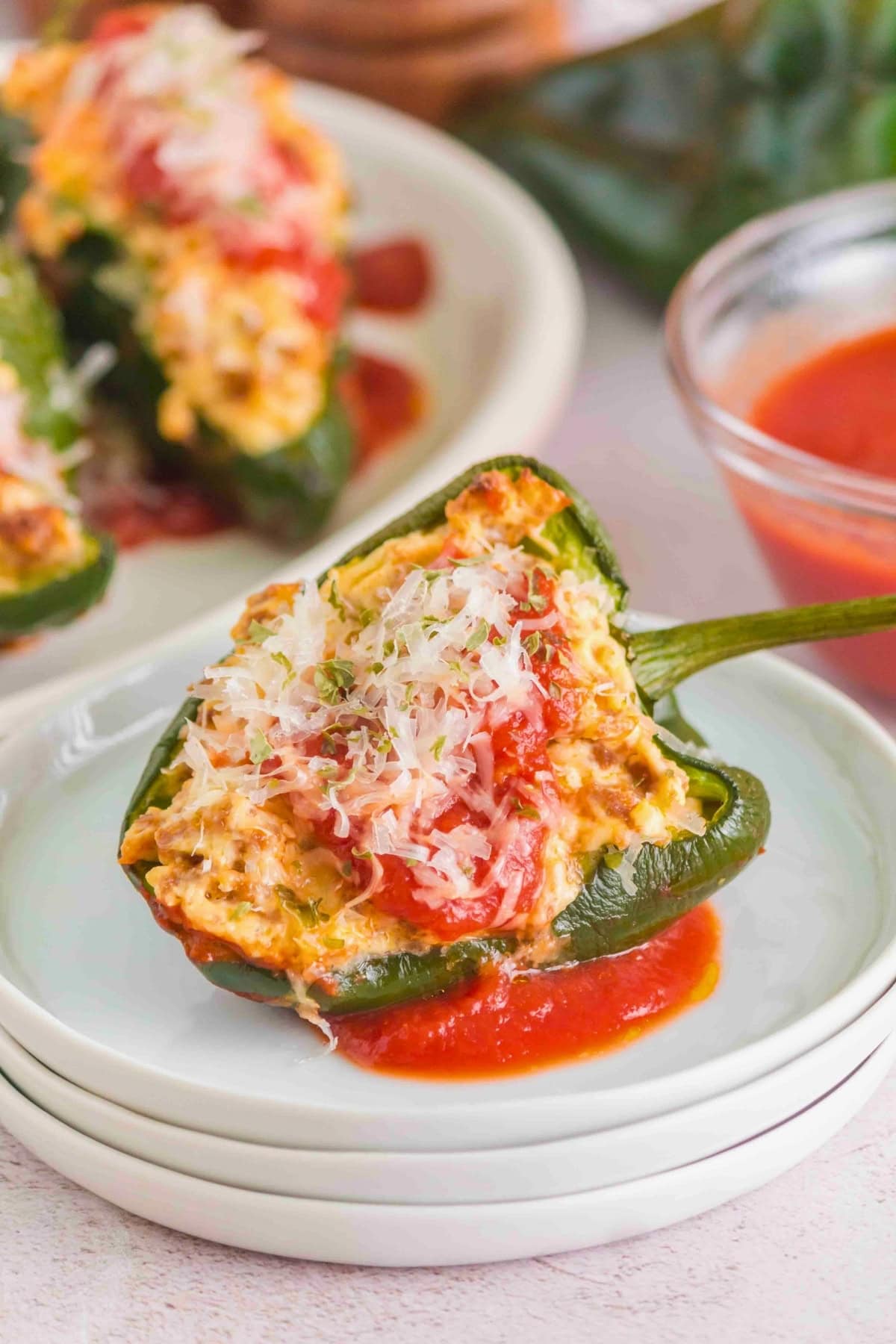 Stuffed poblano pepper topped with cheese and herbs on a plate with tomato sauce.