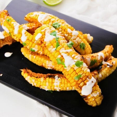 Grilled corn ribs with white sauce and cilantro on a black plate.