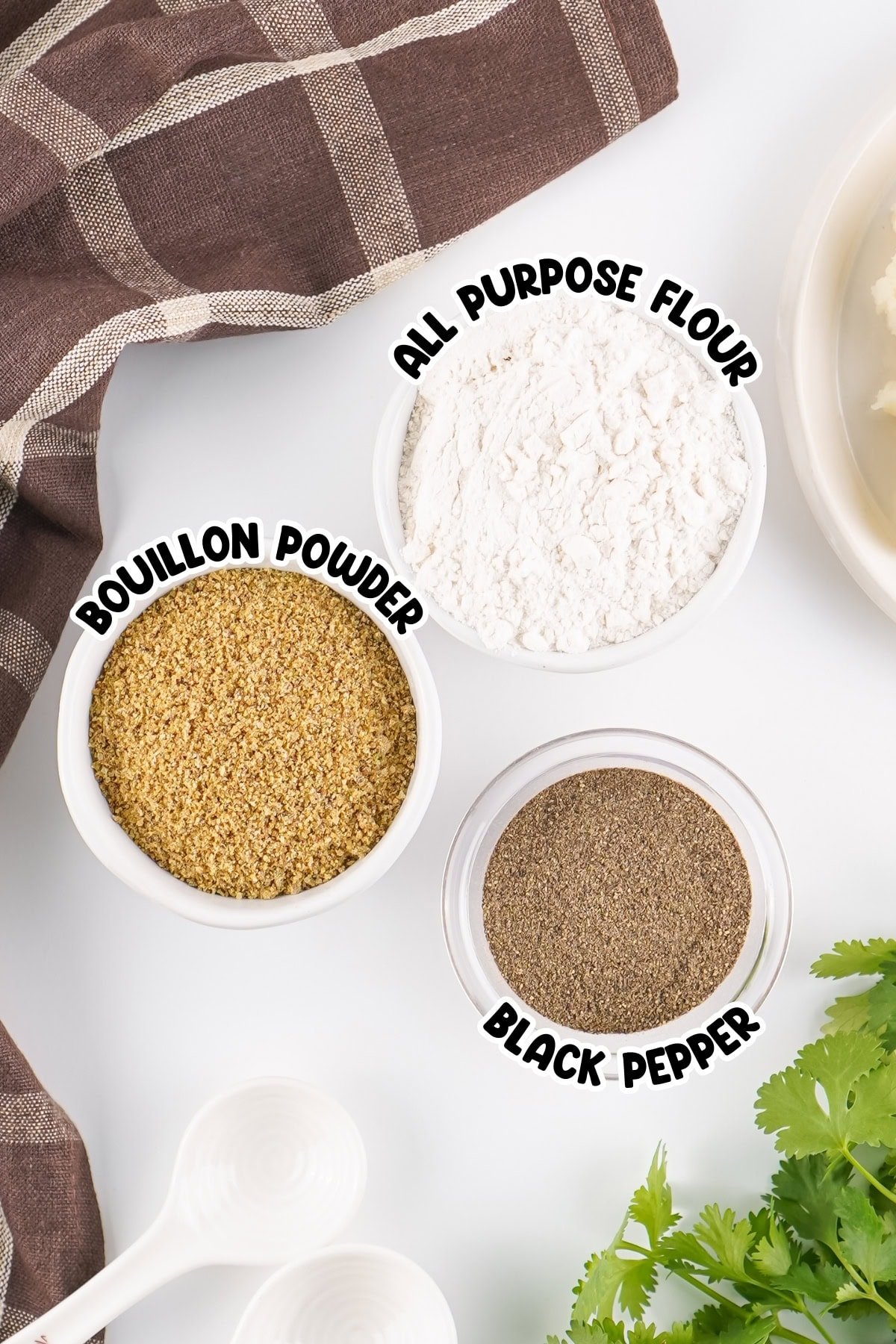 Three labeled bowls containing bouillon powder, flour, and black pepper on a table.