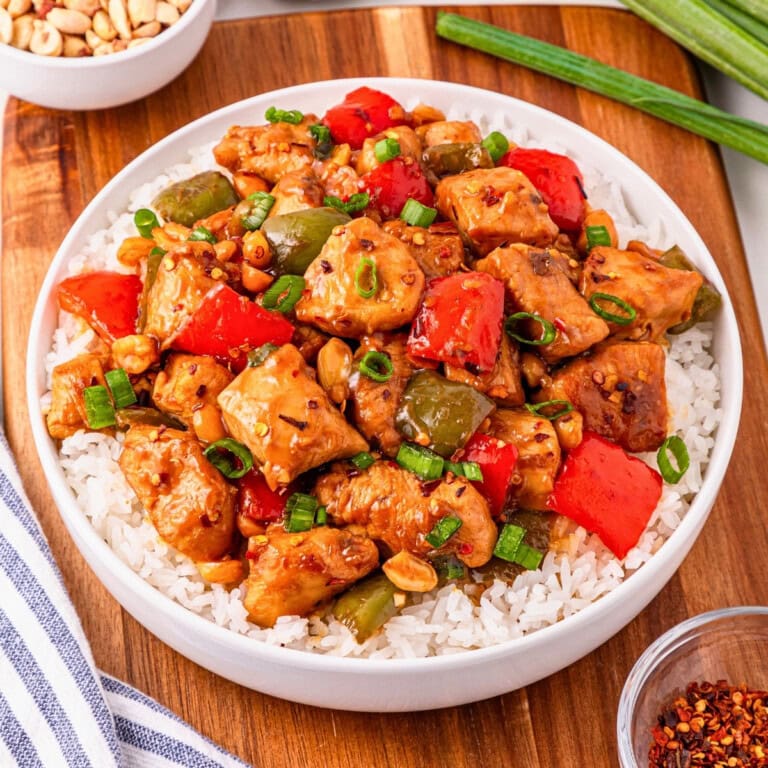 A bowl of rice topped with stir-fried chicken, bell peppers, and green onions.