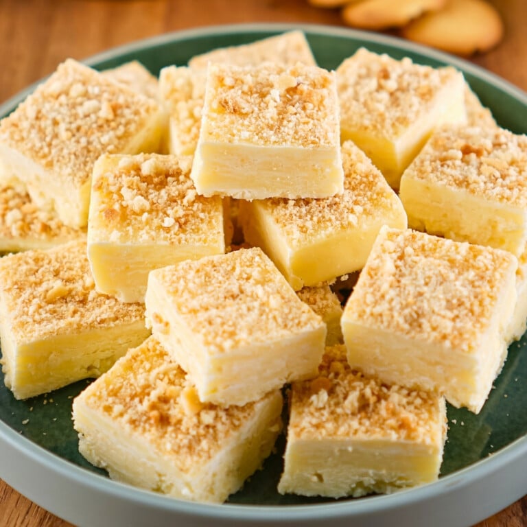 Squares of creamy banana dessert bars with crumbly topping stacked on a green plate.