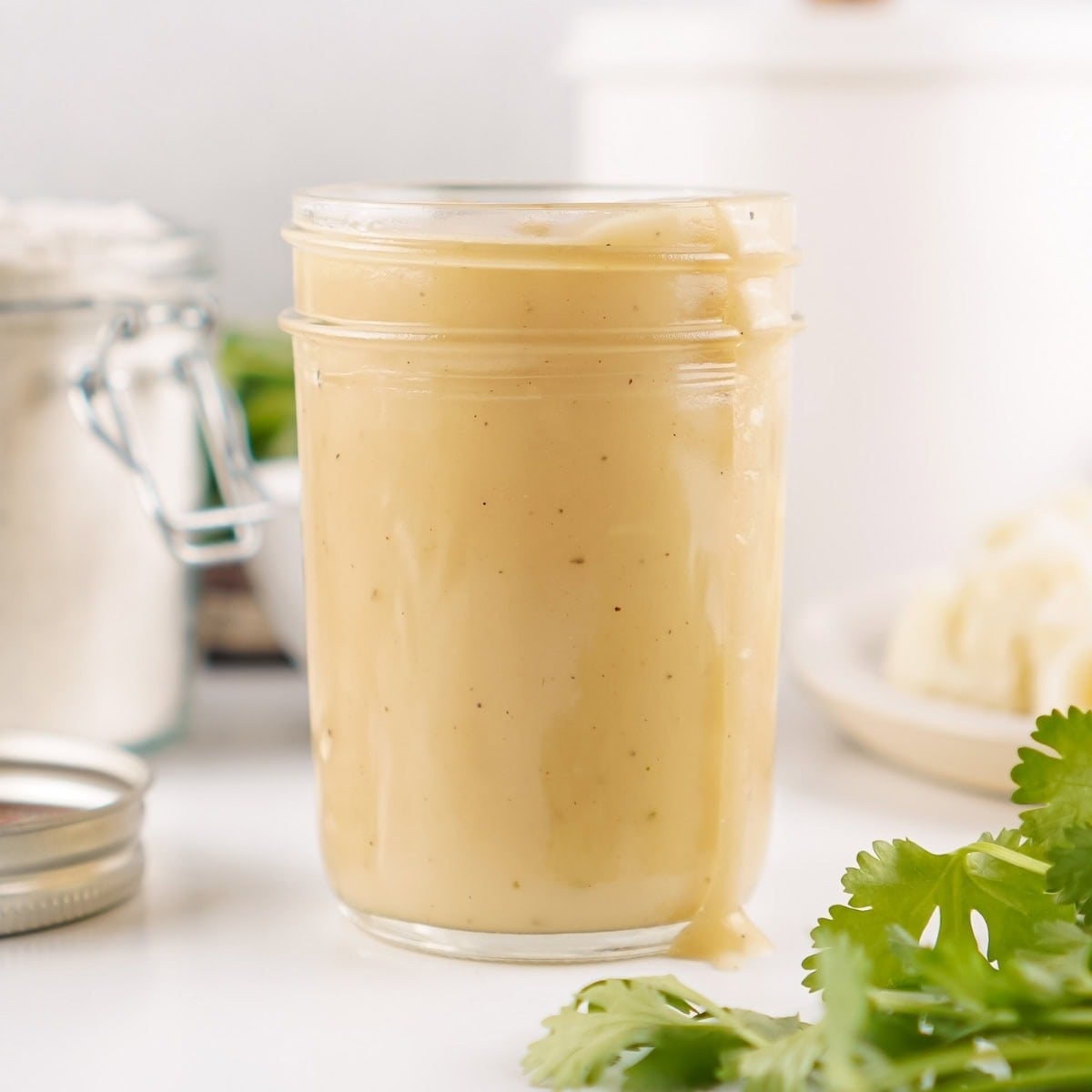 A glass jar filled with gravy, with some sauce dripping down the side.
