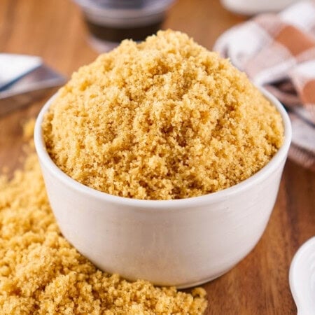A white bowl filled with light brown sugar on a wooden surface.