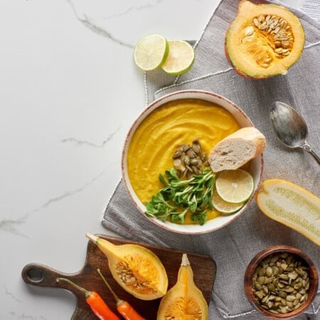 Bowl of pumpkin soup made with pumpkin puree, bread, lime, and seeds on marble.