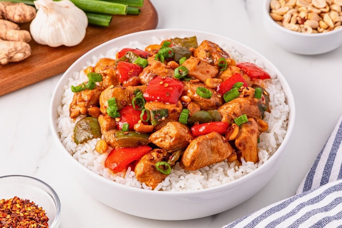A bowl of kung pao chicken with vegetables served over white rice.