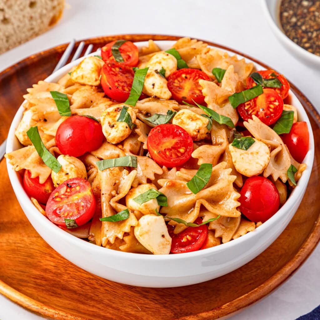 A bowl of bowtie pasta salad with cherry tomatoes, mozzarella, and basil.