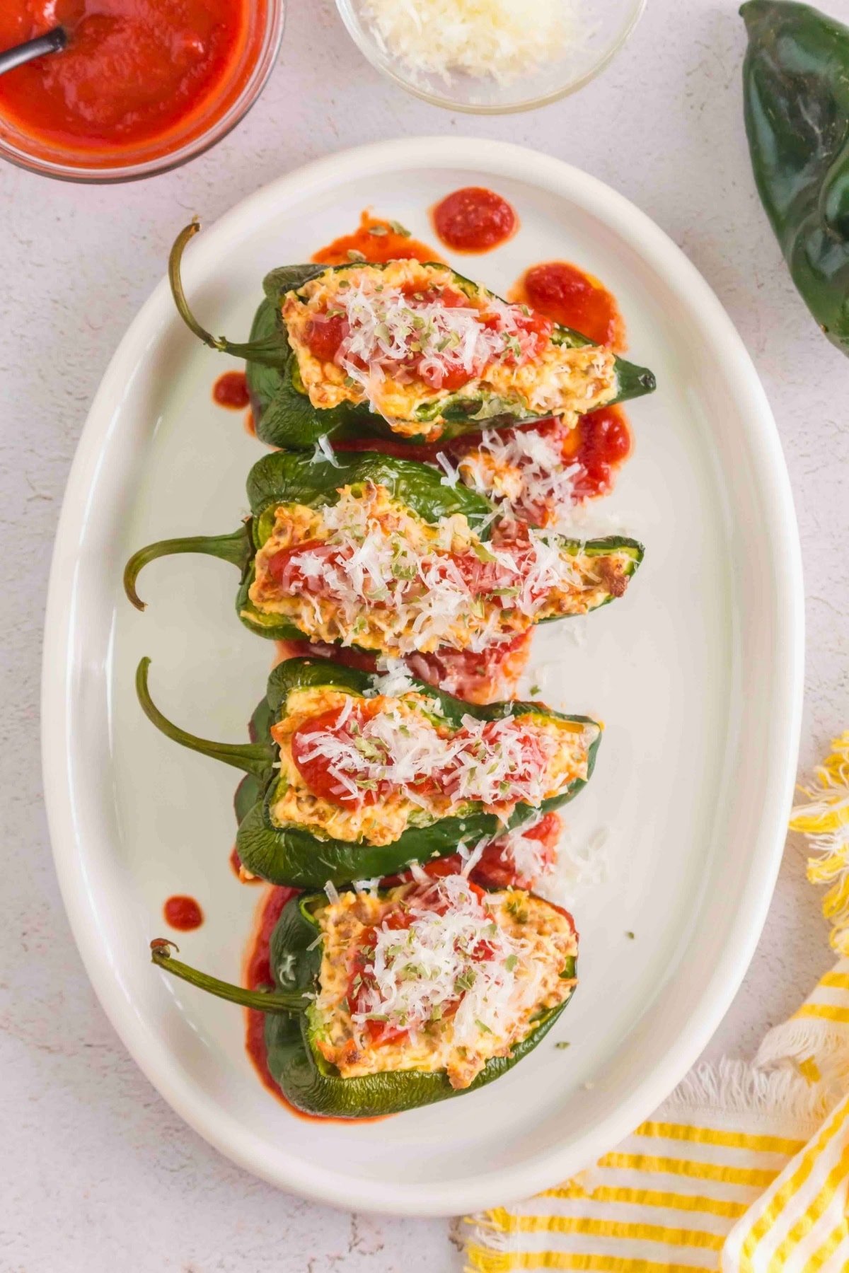 Four stuffed poblano peppers topped with tomato sauce and shredded cheese on a plate.
