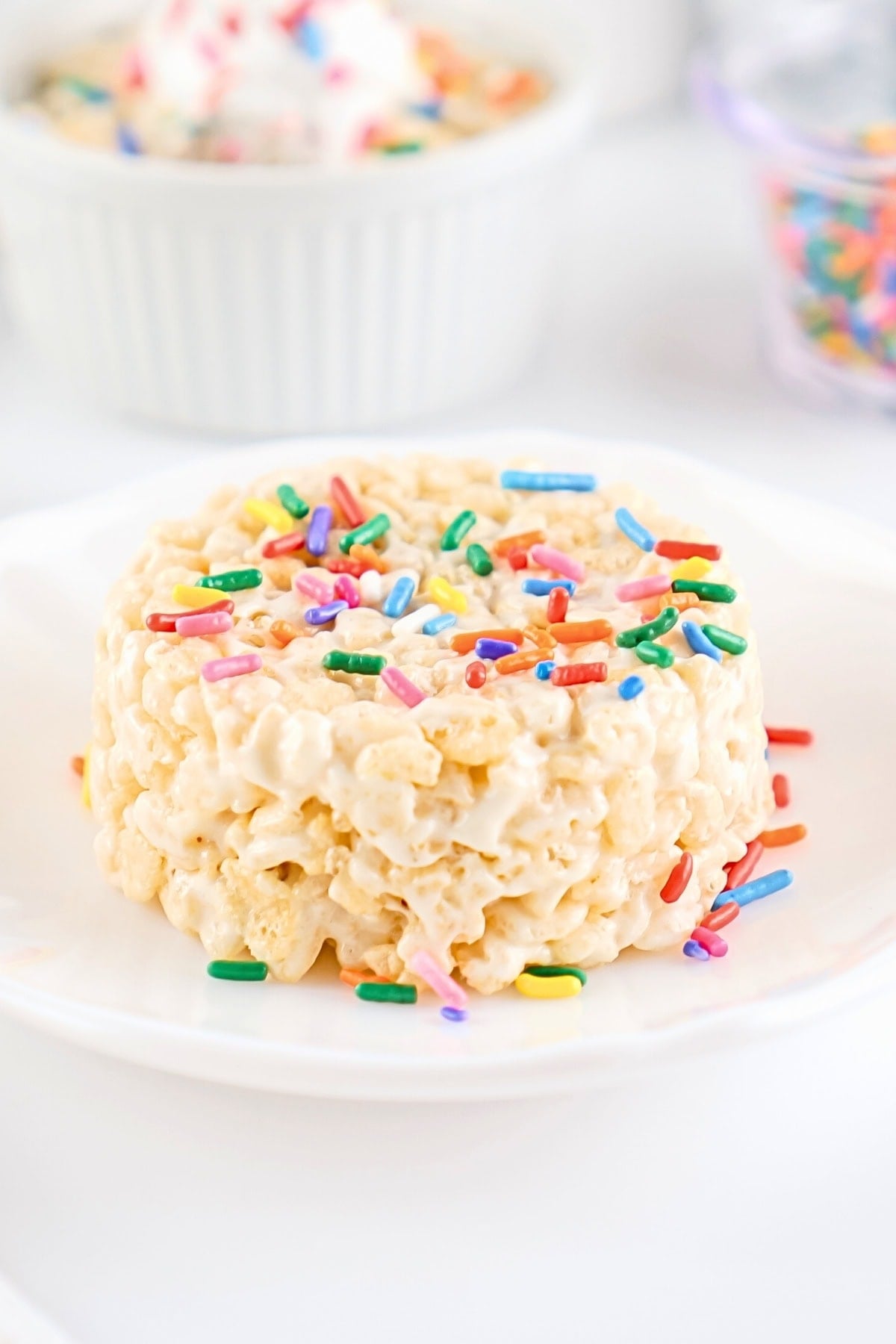 Round rice krispie treat topped with colorful rainbow sprinkles on a plate.