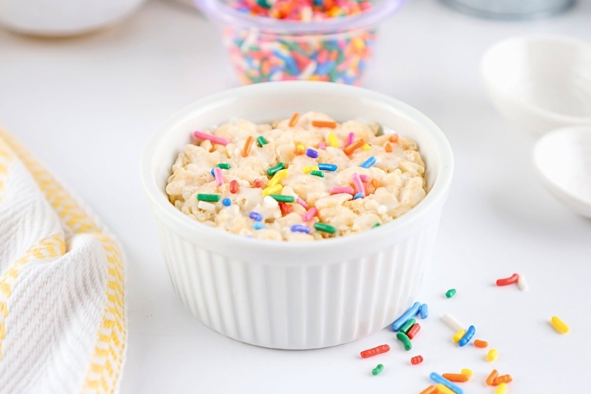 A white ramekin with Rice Krispies treat topped with colorful sprinkles.