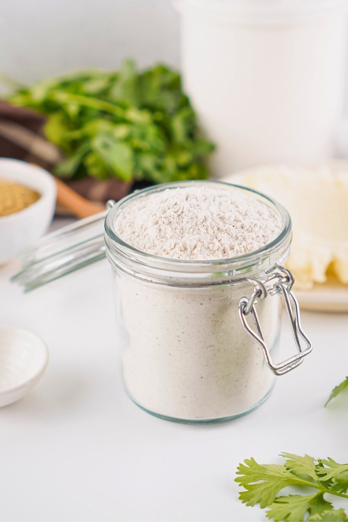 A glass jar filled with gravy mix sits on a white surface with herbs in the background.