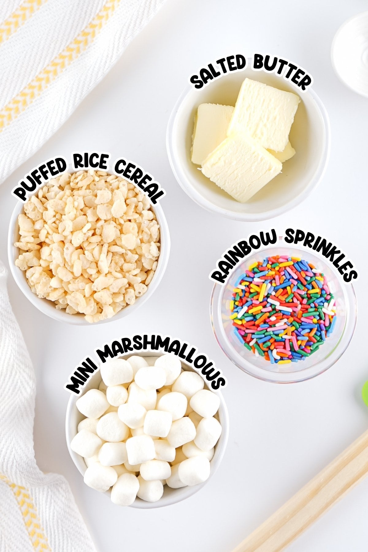 Four bowls with puffed rice cereal, mini marshmallows, salted butter, and sprinkles.