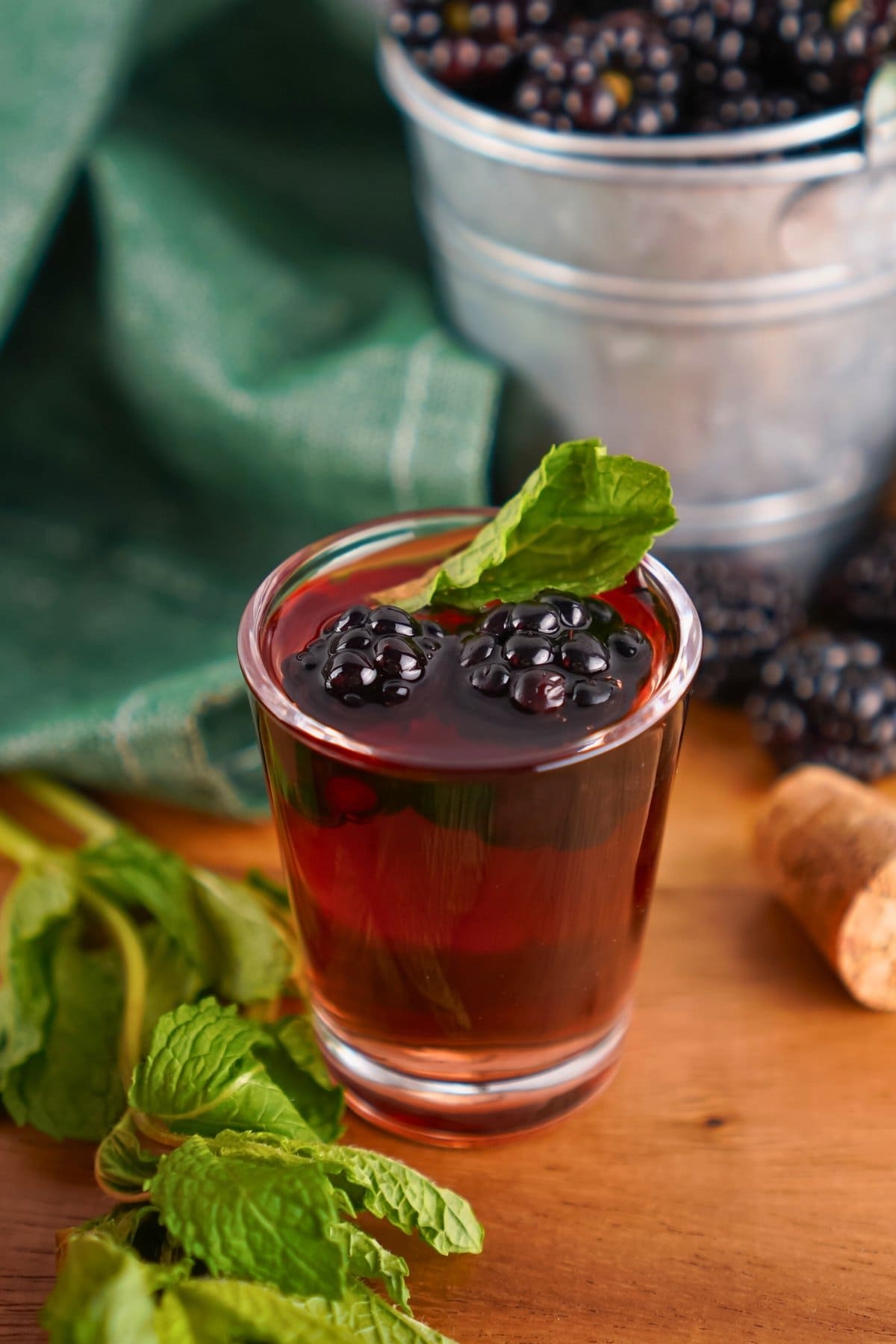 A blackberry cocktail with mint garnish sits on a wooden table.