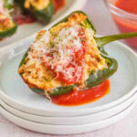Stuffed poblano pepper topped with cheese and tomato sauce on a white plate.