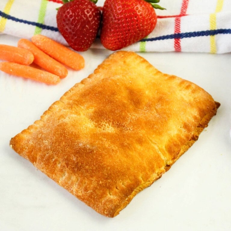 Golden-brown pastry on a plate with strawberries and baby carrots nearby.