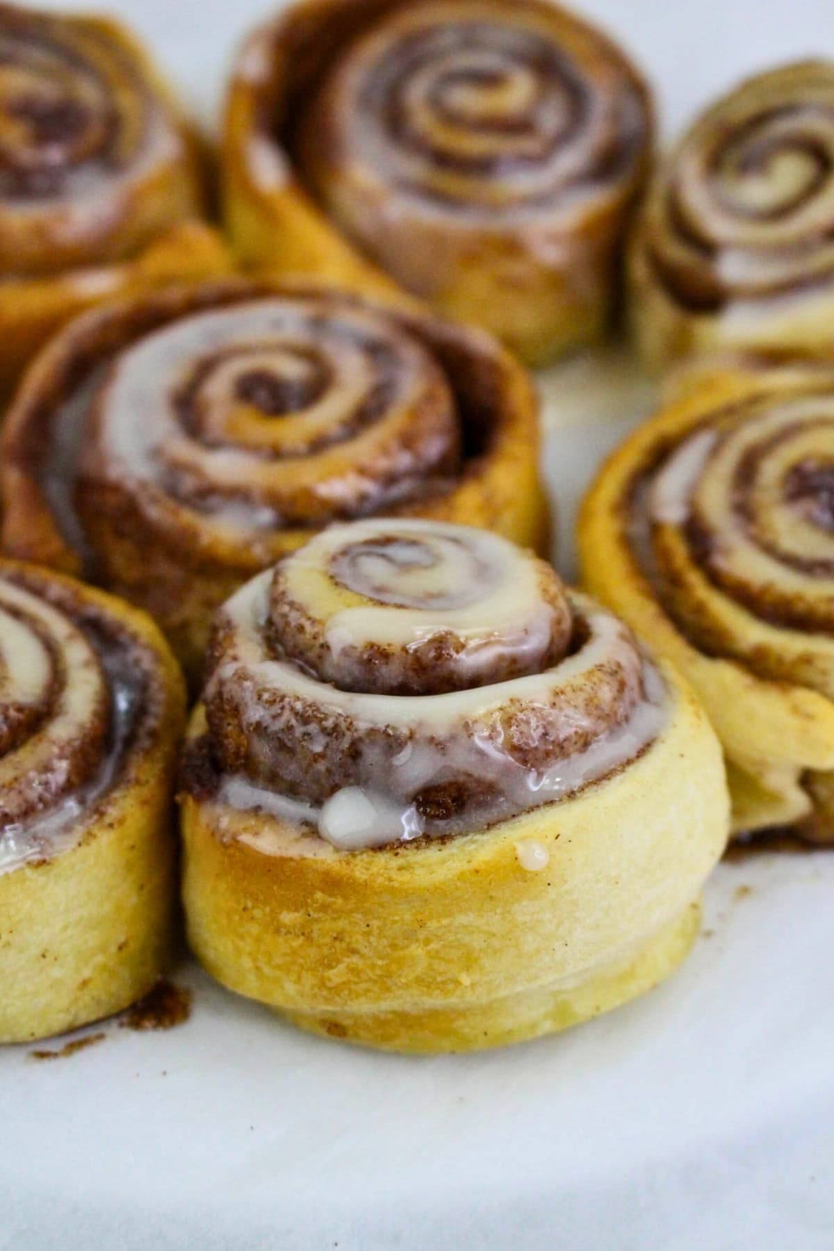 Cinnamon rolls with icing on top, arranged on a white surface.