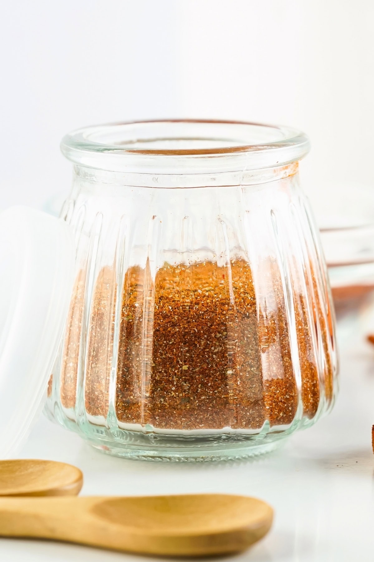 Glass jar filled with red spice mix, with wooden spoons in the foreground.