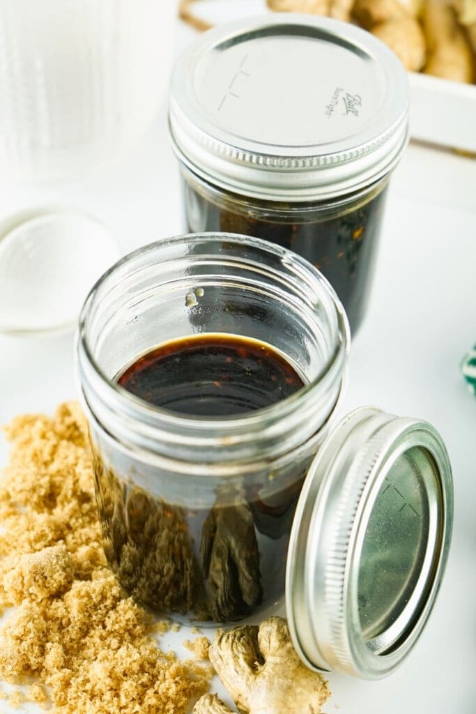 Two jars of Teriyaki Sauce with brown sugar and ginger on a white surface.