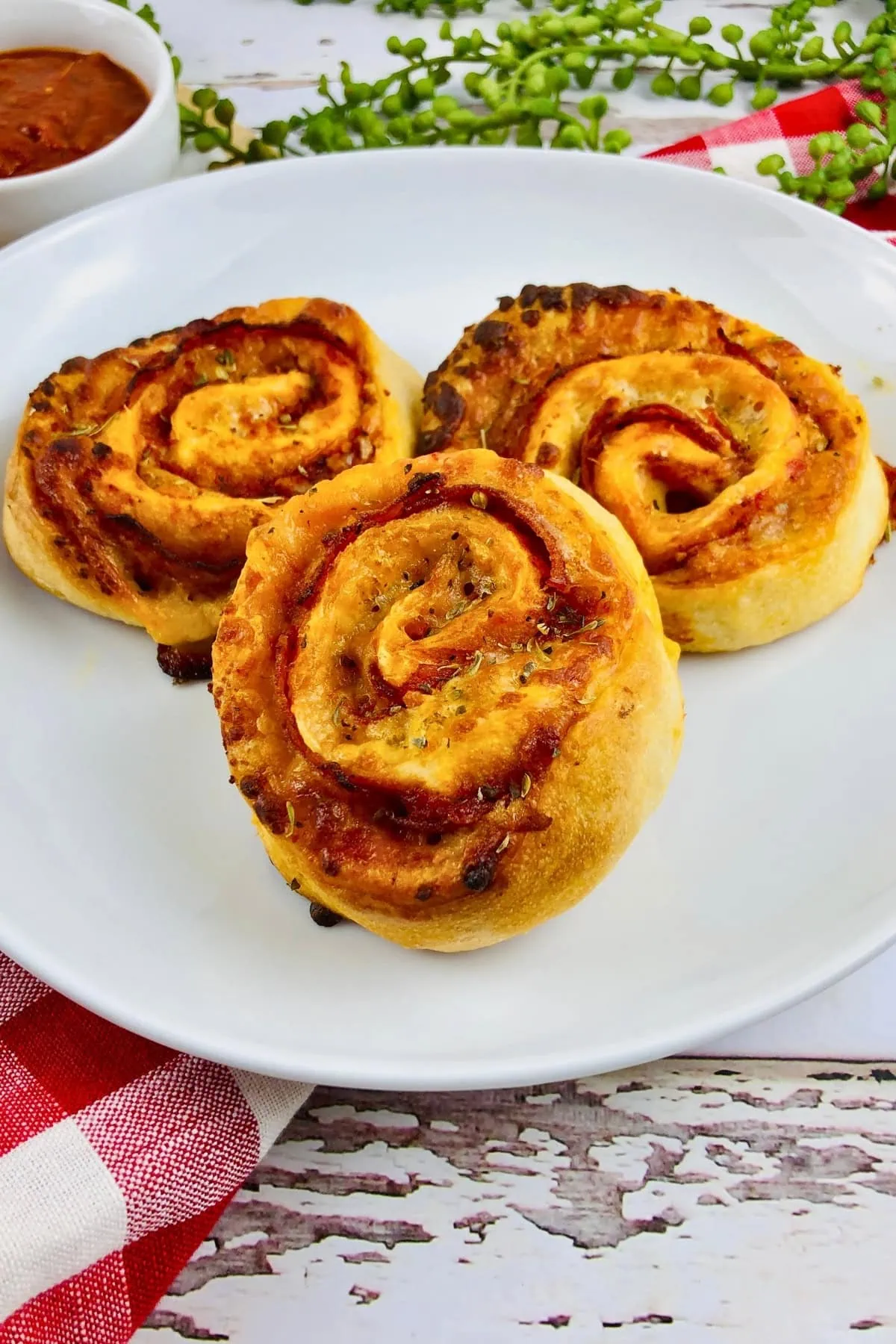 Three pizza pinwheels on a white plate with a red and white napkin.