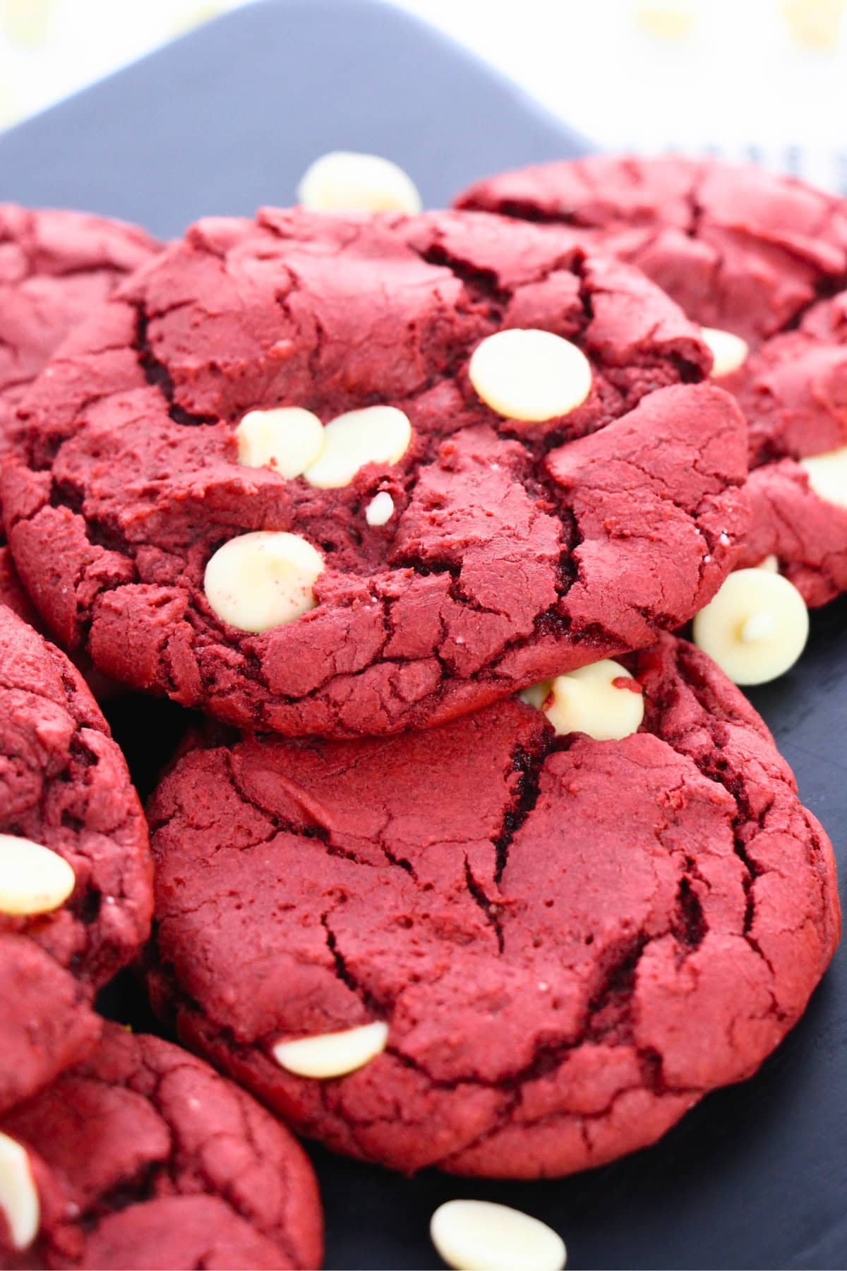 Red velvet cookies with white chocolate chips stacked on a dark serving plate.