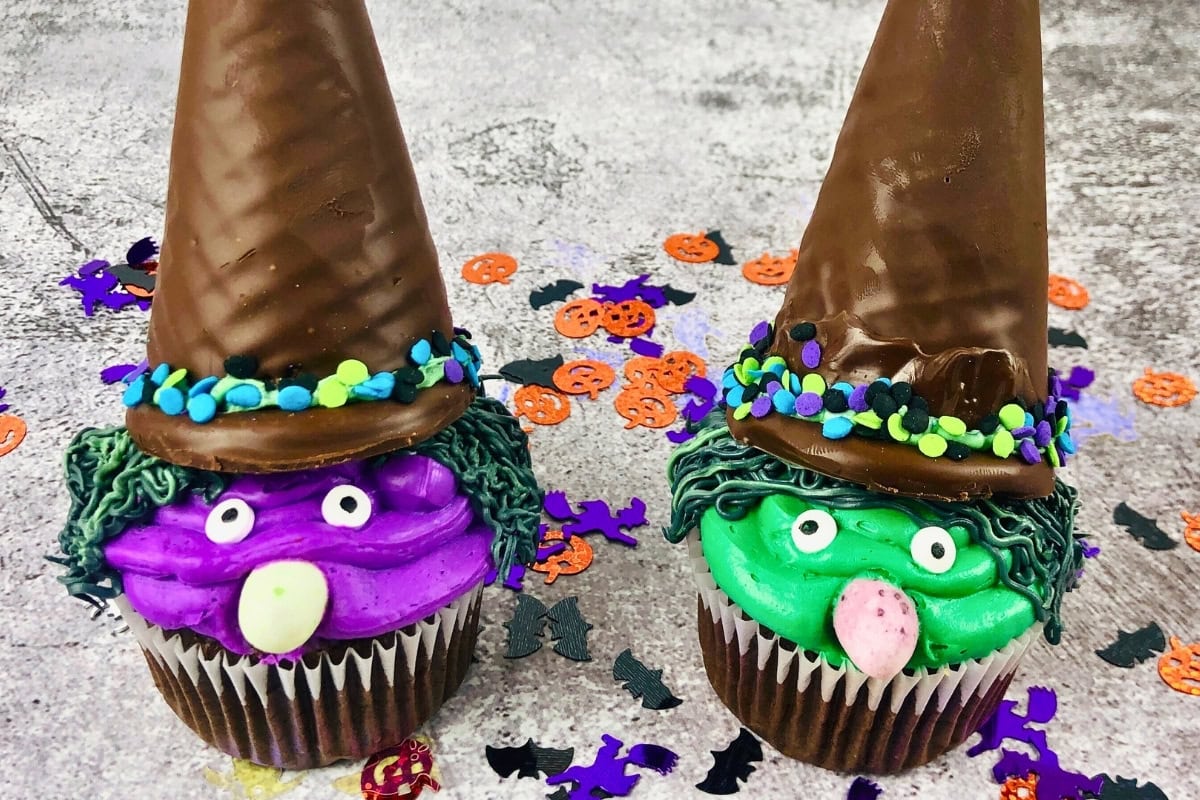 Two cupcakes decorated as colorful witches with ice cream cone hats and candy faces.