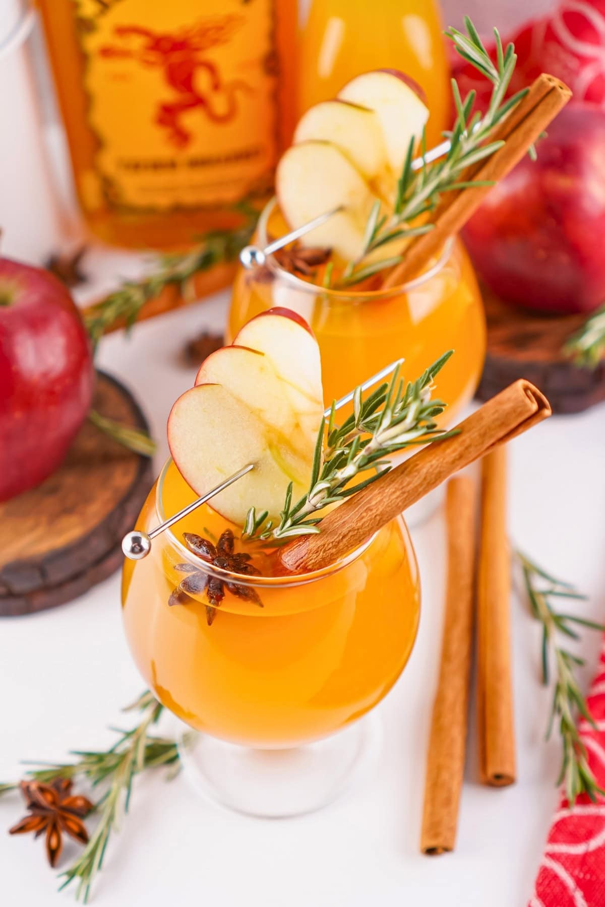 Apple cocktails with cinnamon sticks, rosemary, and apple slices for garnish.
