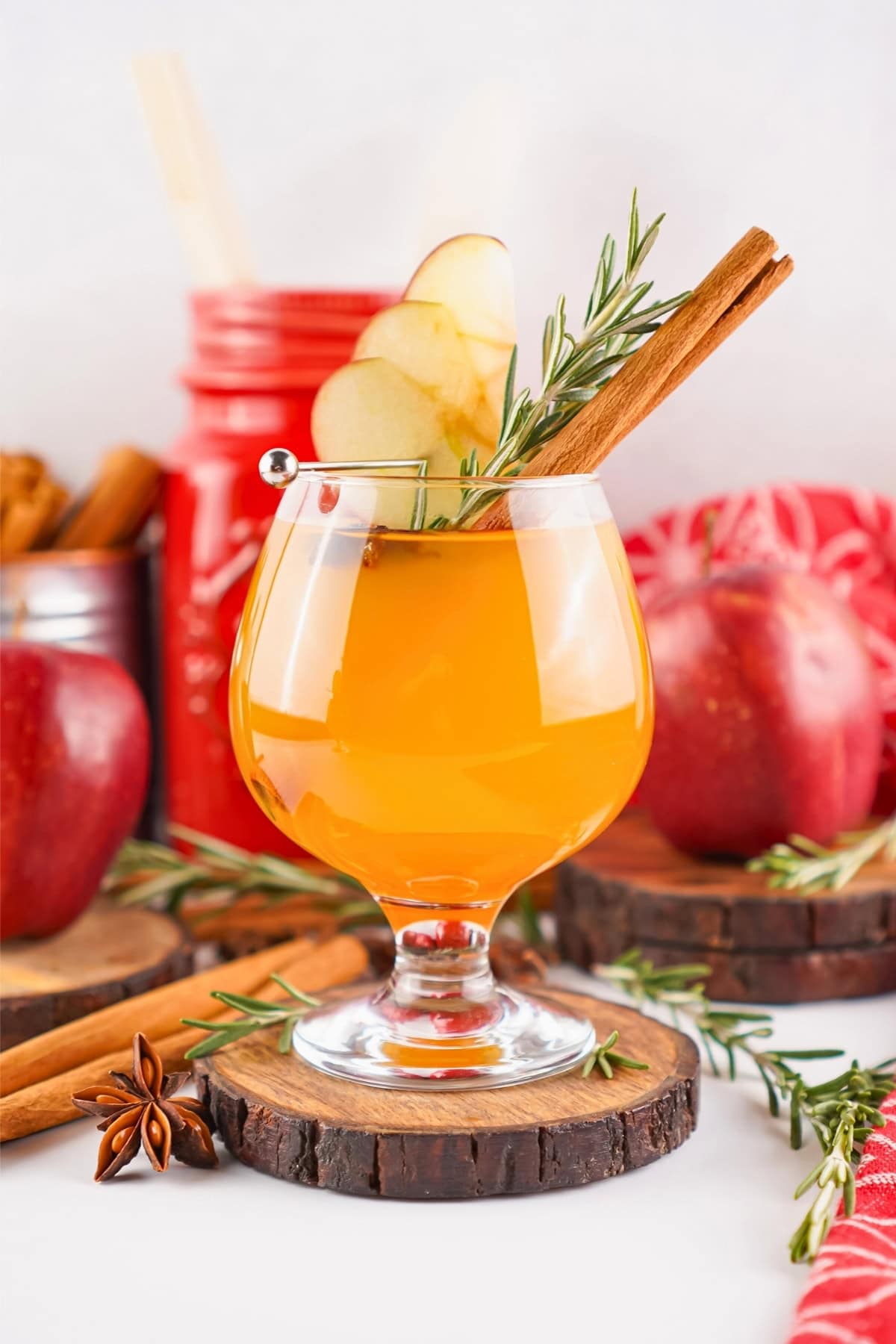 A spiced apple cocktail garnished with apple slices, rosemary, and cinnamon.