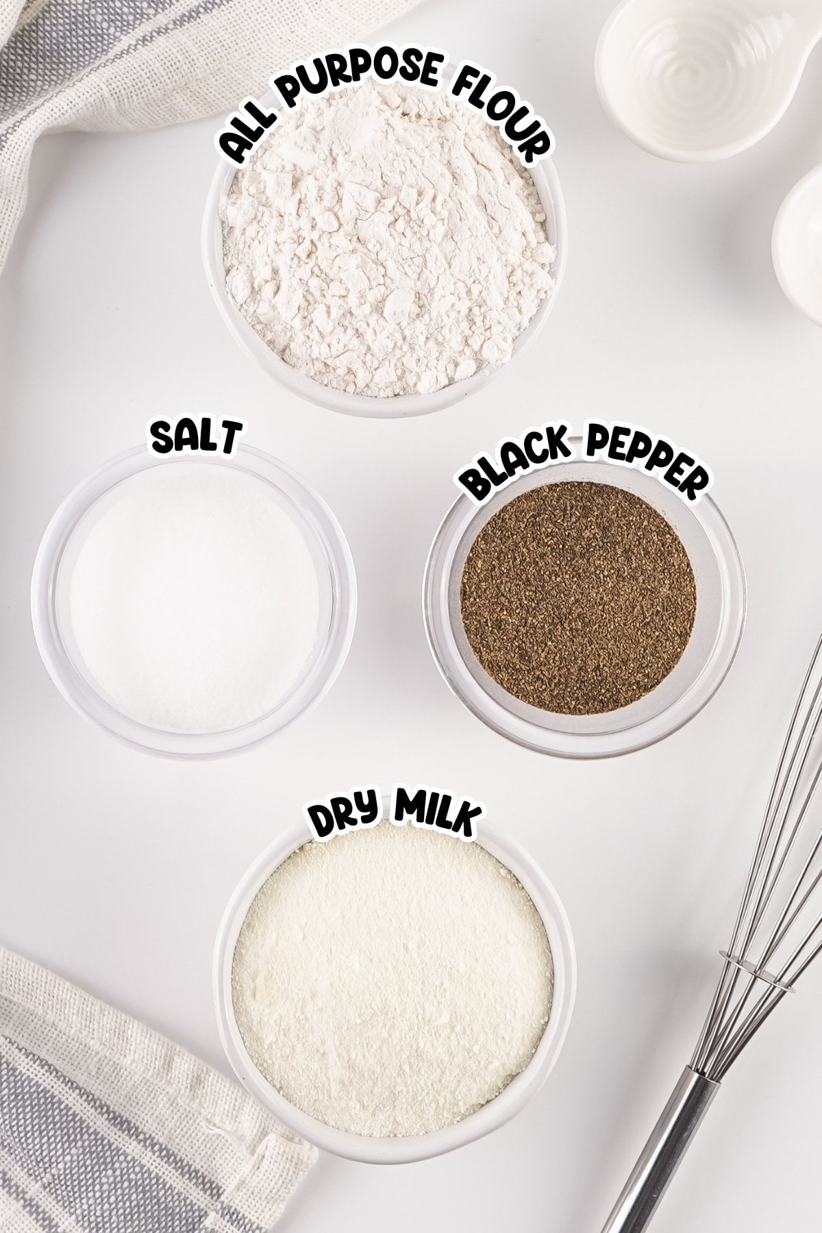 Four labeled bowls with flour, salt, black pepper, and dry milk on a white surface.