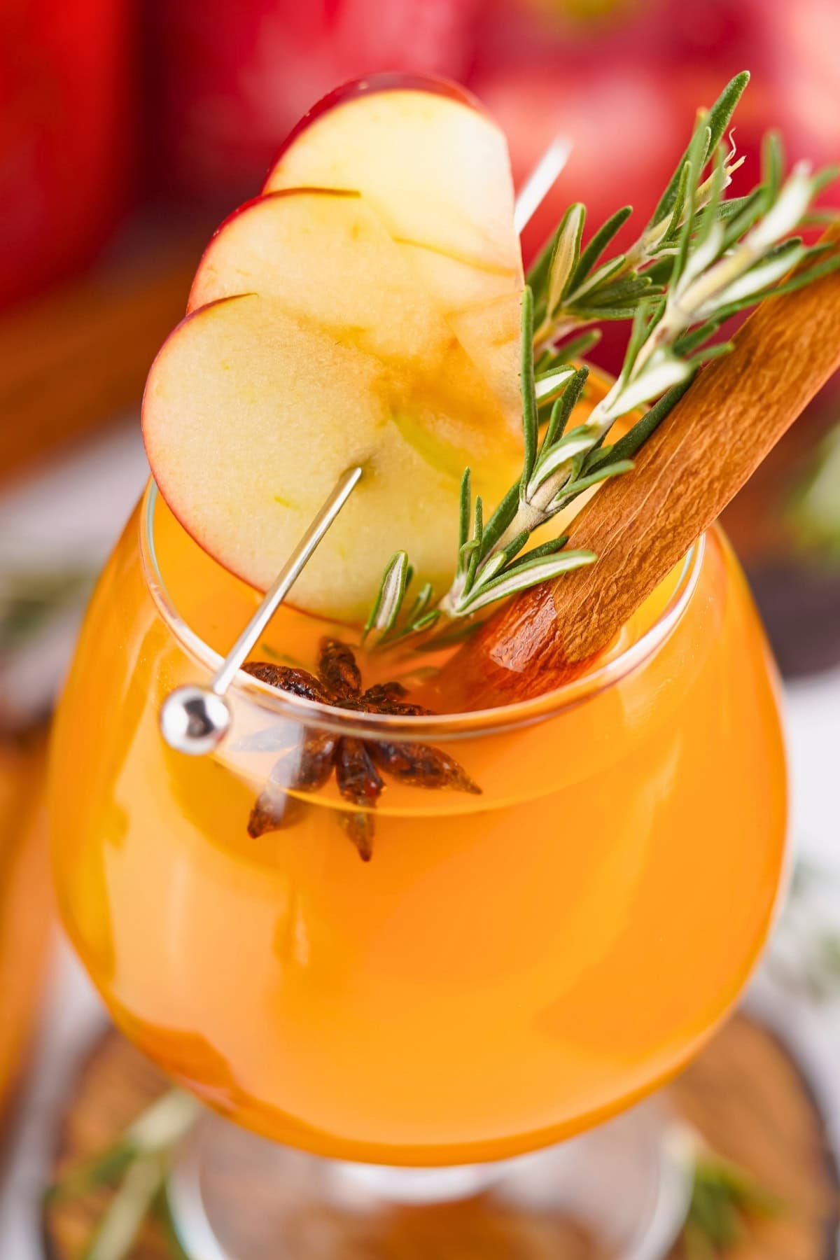 Orange cocktail garnished with apple slices, rosemary, star anise, and cinnamon stick.