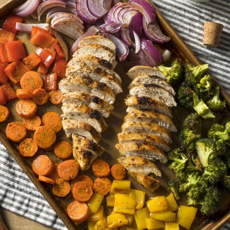 Sliced chicken breast with sheet pan vegetables: carrots, peppers, onions, broccoli.
