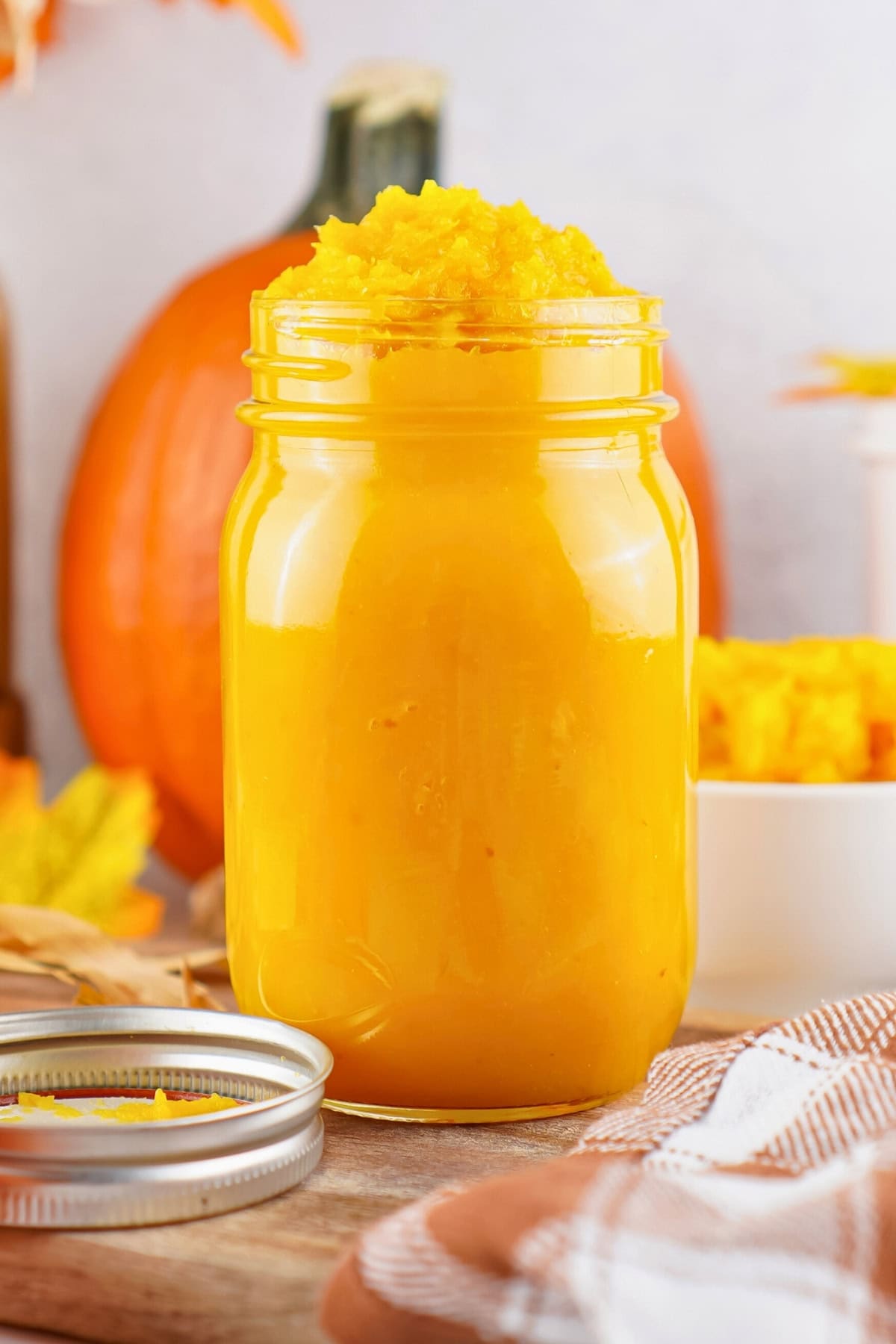 A jar of bright orange pumpkin puree with a lid and pumpkins in the background.